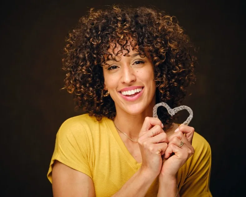 Patient smiling and holding up their invisalign.